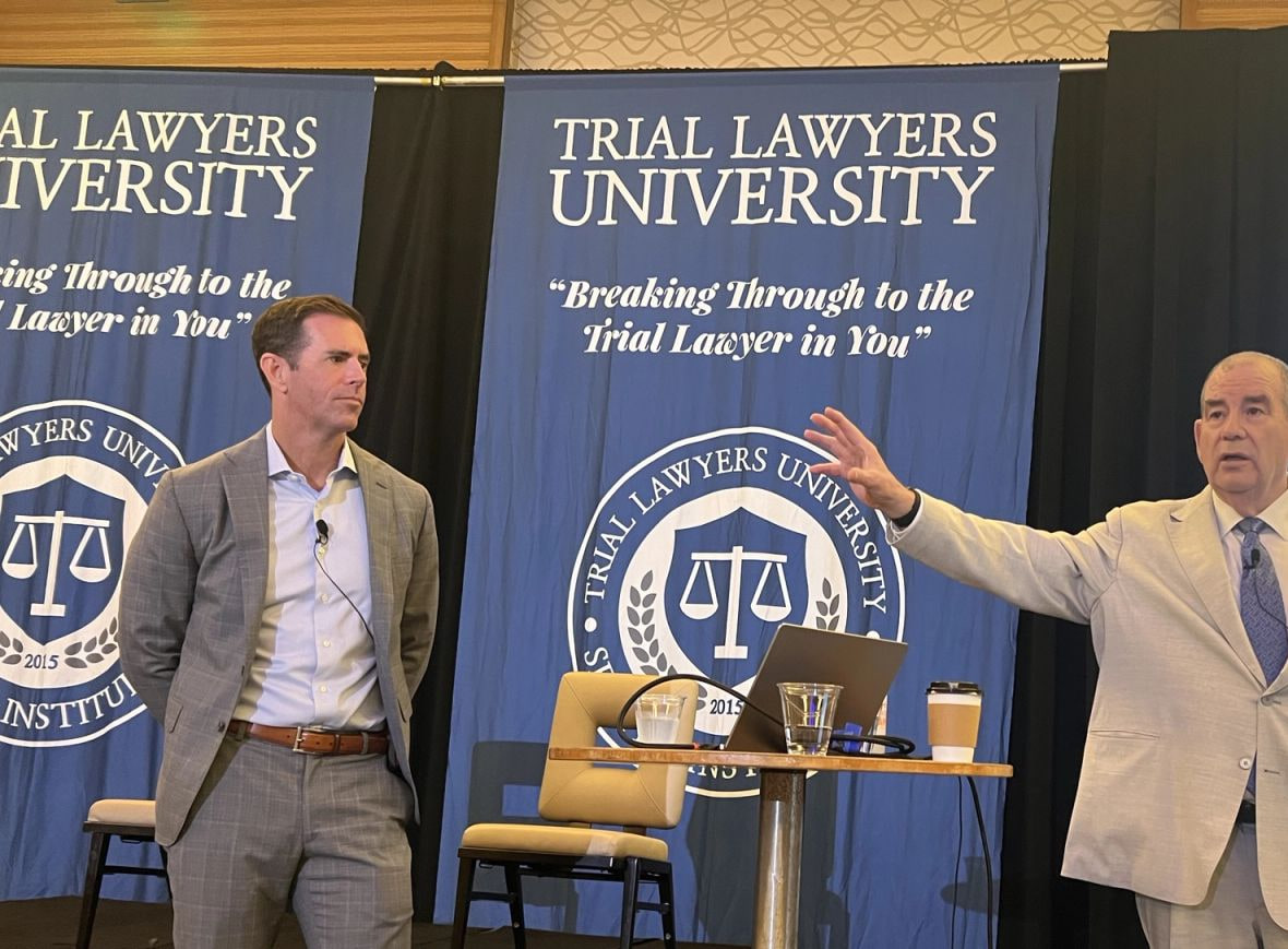 Two Trial Lawyers University faculty on stage in front of the TLU banners
